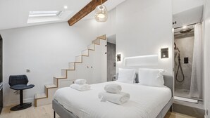 A modern bedroom with a large bed, a chair, a staircase, and a shower area. - Le Rempart Duplex - Au coeur du Vieil Antibes (Antibes)