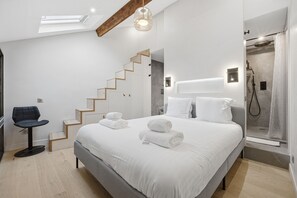 Ein modernes Schlafzimmer mit einem großen Bett, einem Sessel, einer Treppe und einem Duschbereich.