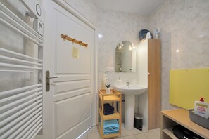 Un bany amb una porta blanca, un lavabo, un mirall, una barra de tovalloles i una estant amb productes de tocador.