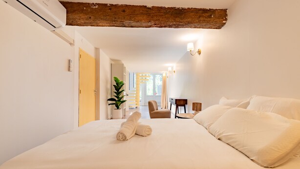 A bedroom with a bed, a wooden ceiling beam, a potted plant, and a chair. - Le Resticas - Triplex climatisé (Rustiques)