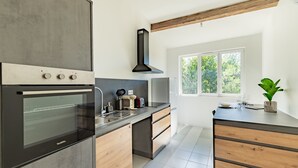 A modern kitchen with a built-in oven, a sink, and a window providing natural light. - Le Resticas - Triplex climatisé (Rustiques)