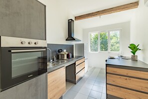 A modern kitchen with a built-in oven, a sink, and a window providing natural light. - Le Resticas - Triplex climatisé (Rustiques)