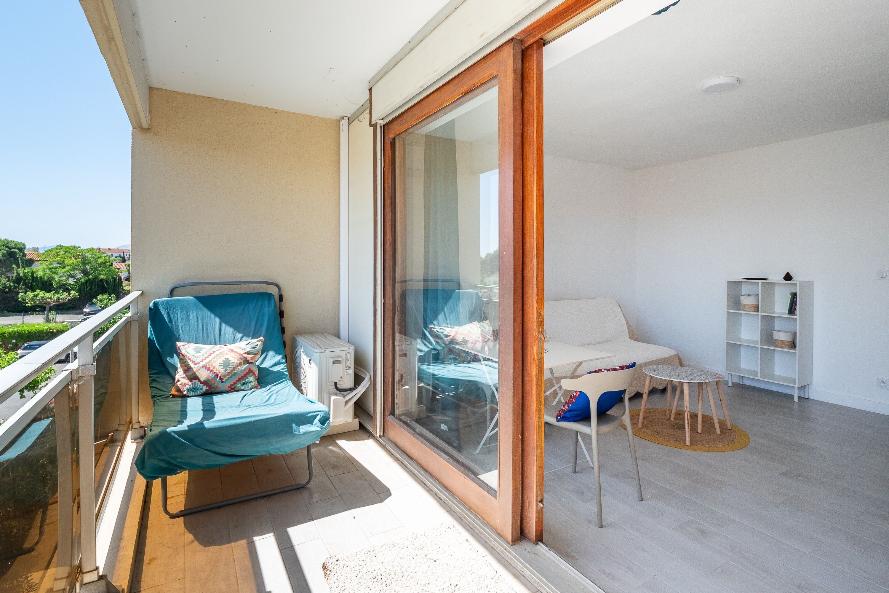 A balcony with a sofa and a chair, a small table, and a white shelving unit.