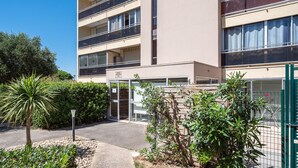 A multi-story building with balconies, a gated entrance, and a small garden area with a palm tree. - Le Refuge de Canet - Studio climatisé (Canet-en-Roussillon)