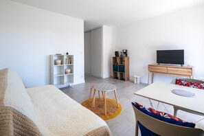 Ein modernes Wohnzimmer mit einer Couch, einem Esstisch, einem Fernseher und einem kleinen Hocker.