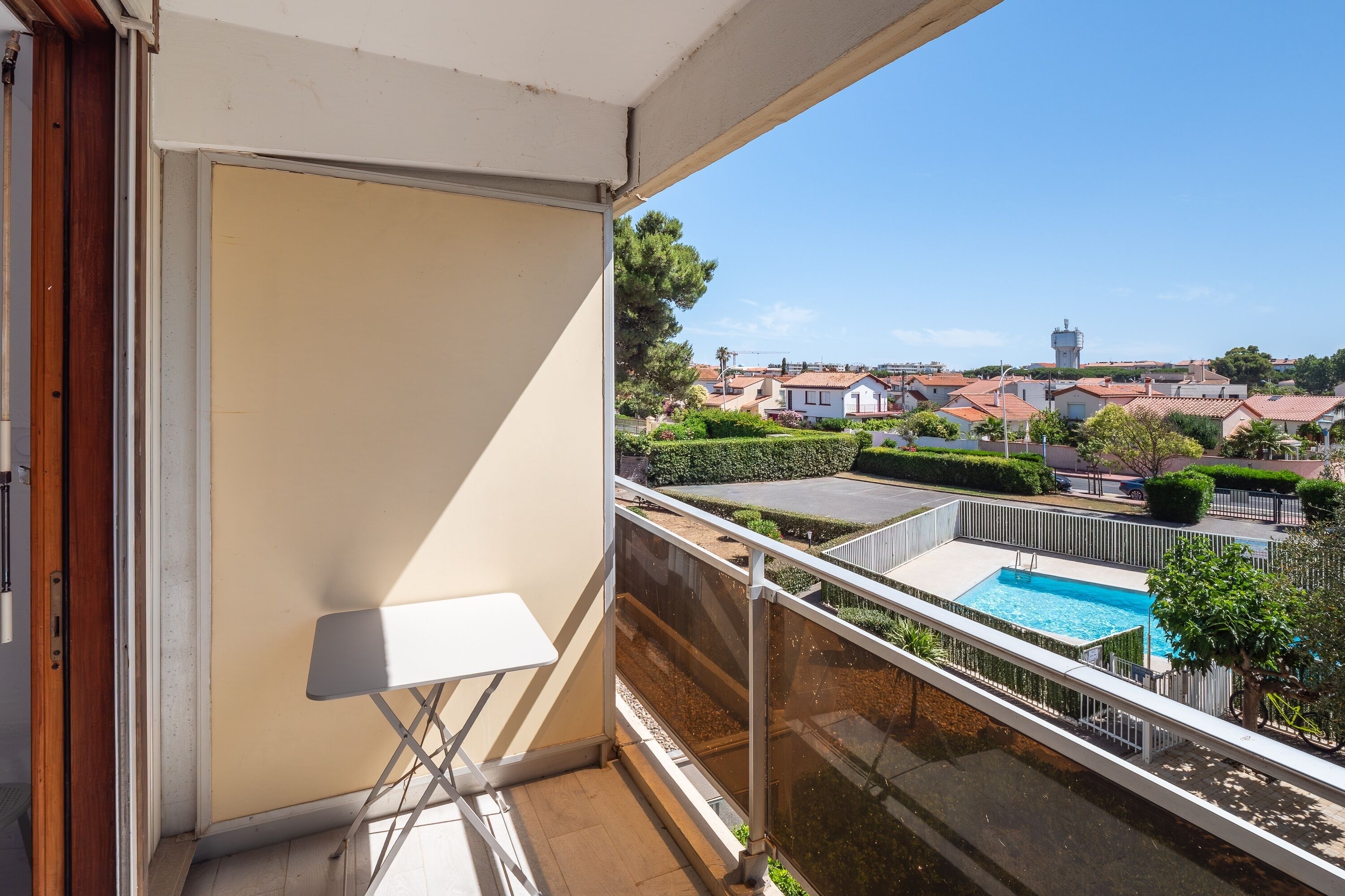 Un balcon donnant sur une piscine, une table blanche et une porte.