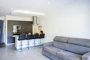 Eine moderne Küche mit einer zentralen Kochinsel, Barhocker und einem grauen Sofa.