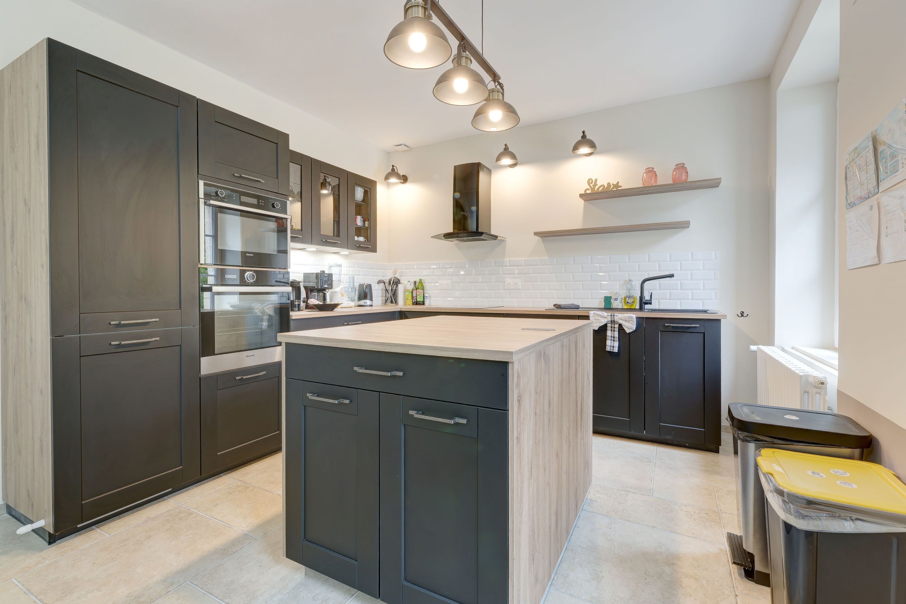 A modern kitchen with dark cabinetry, a central island, and pendant lighting.