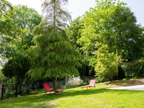 Ein Garten mit zwei roten Stühlen, einem Holzzaun und verschiedenen Bäumen.