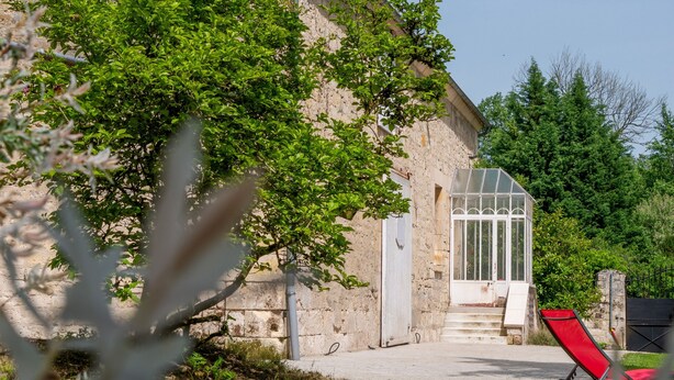 A stone building with a glass door, a red chair, and a tree in the foreground. - Les Clés de Censibele - Charmant gîte pour 12 (Braye)