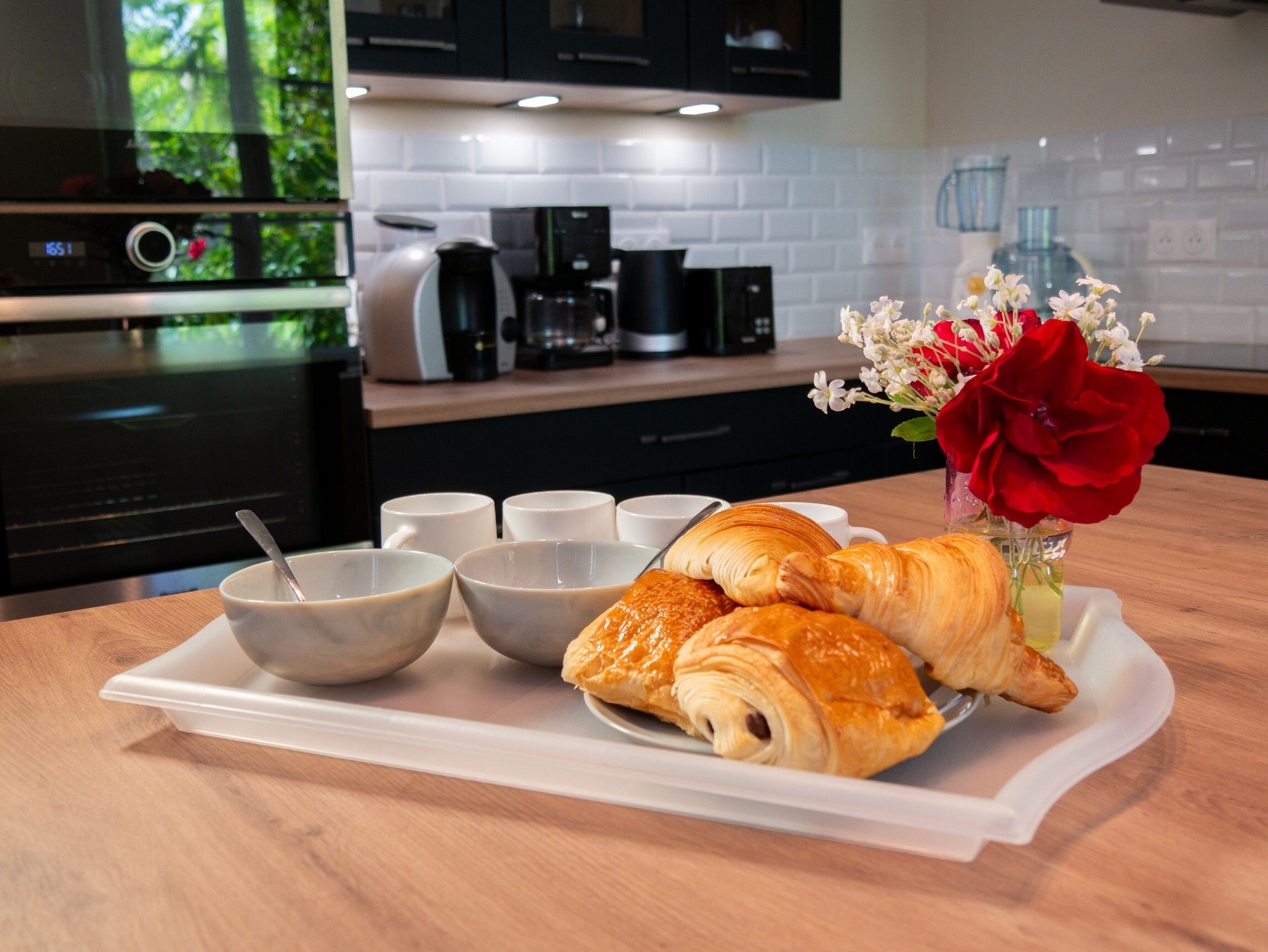 Un plateau contenant des croissants, des bols et un vase rempli de fleurs, le tout posé sur une table en bois dans une cuisine.