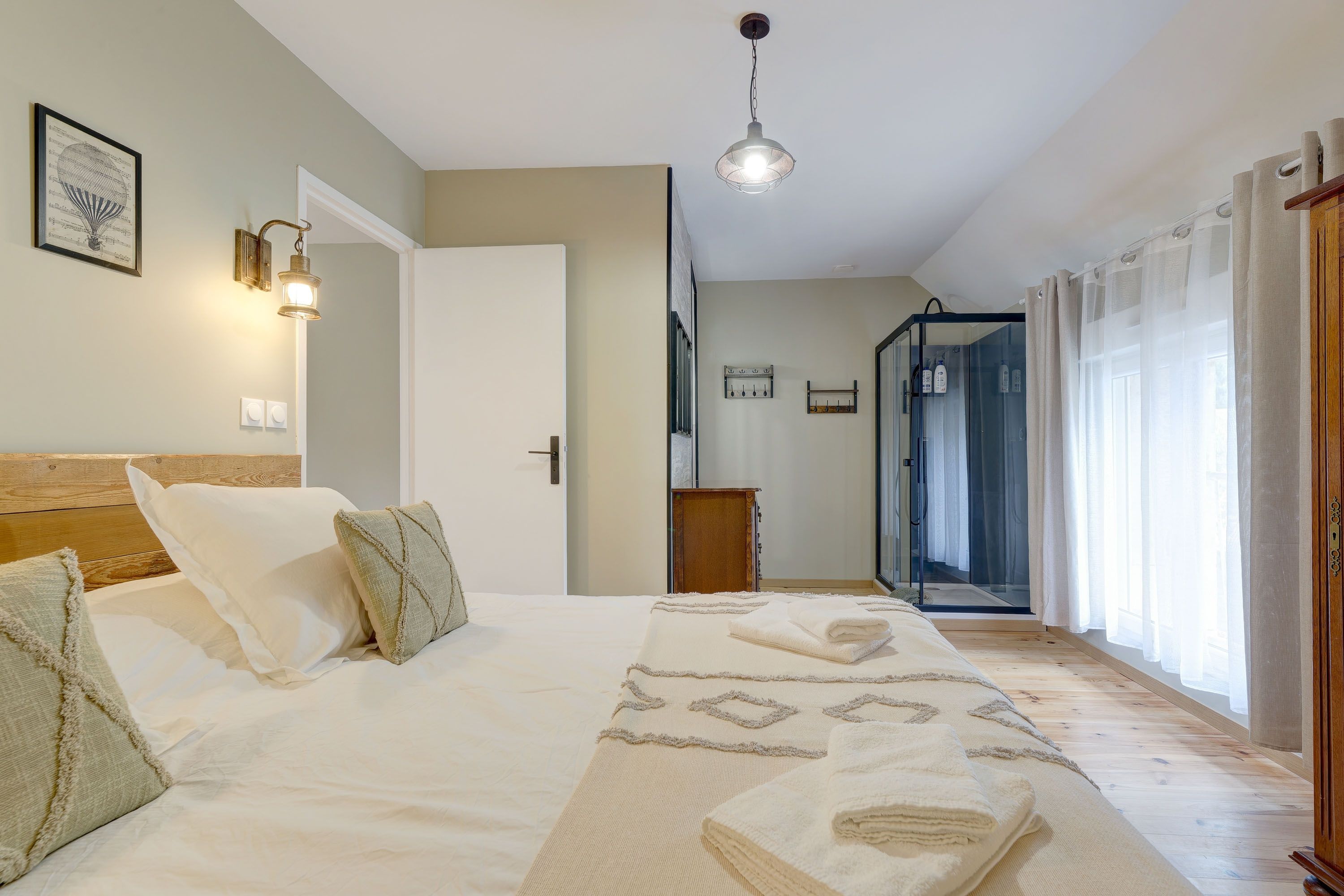 Ein Schlafzimmer mit einem Bett, Nachttischlampen, einer Tür, einem Spiegel und einer Duschkabine.