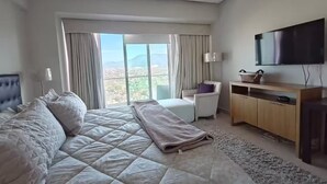 Een slaapkamer met een groot bed, een televisie, een bureau en uitzicht op een stadsbeeld.