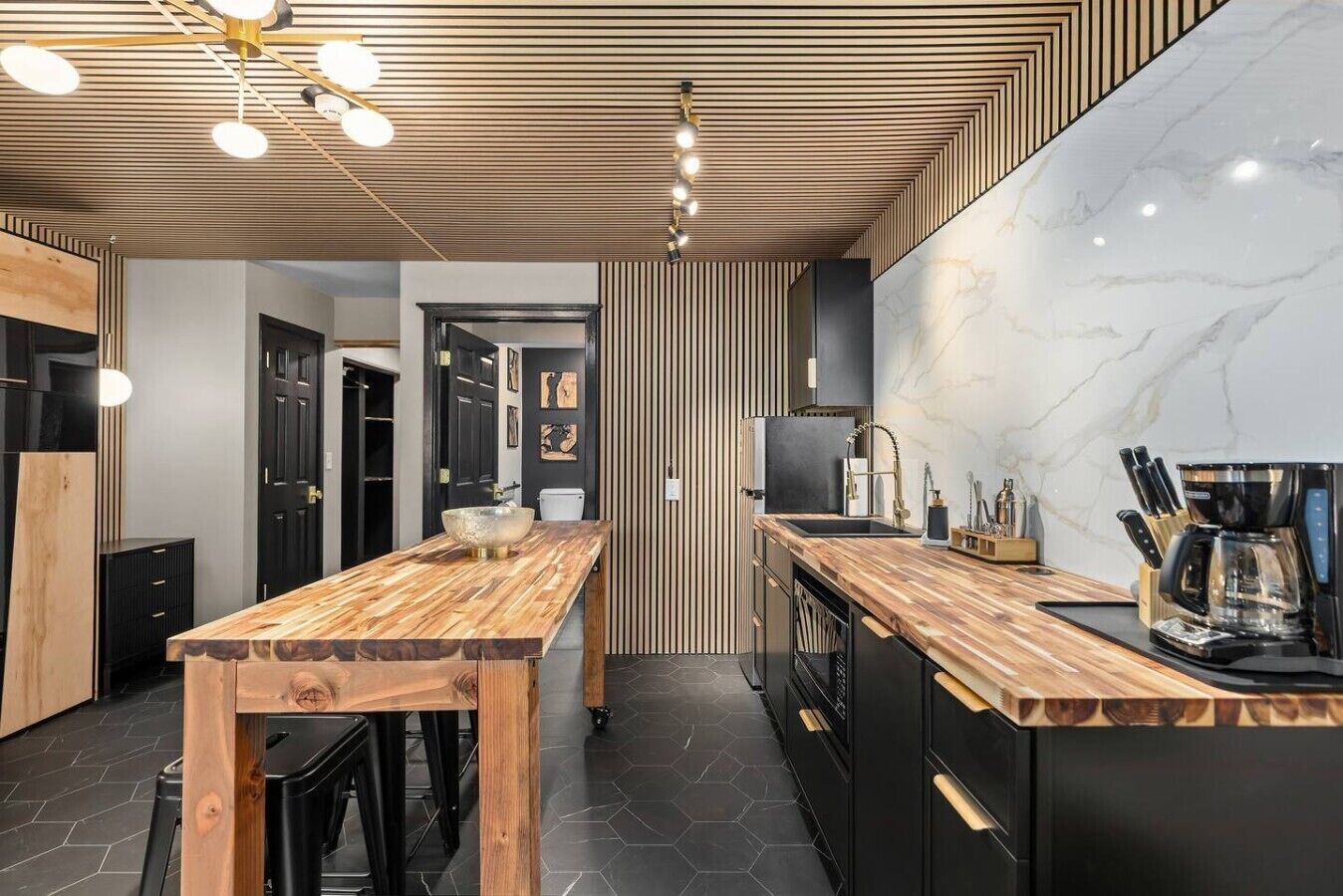 A modern kitchen with a wooden island, black cabinets, and a marble backsplash.