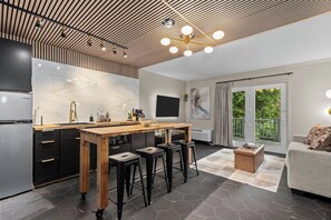 Une cuisine moderne avec un îlot central en bois, des tabourets de bar noirs et une grande fenêtre donnant sur un jardin.