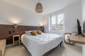 Ein Schlafzimmer mit einem großen Bett, Nachttischlampen, einem Holznachttisch, einem Schreibtisch mit Computer und einem Fenster mit Blick.