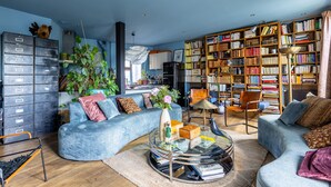 Ein Wohnzimmer mit blauem Sofa, Bücherregal und einer Pflanze.