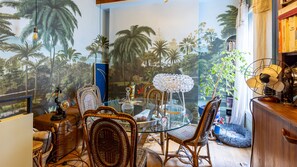 A room with a glass table surrounded by wicker chairs, a decorative lamp, and a bookshelf with books. - Montmartre View - Appt avec vue sur le Sacré-Cœur (Paris)