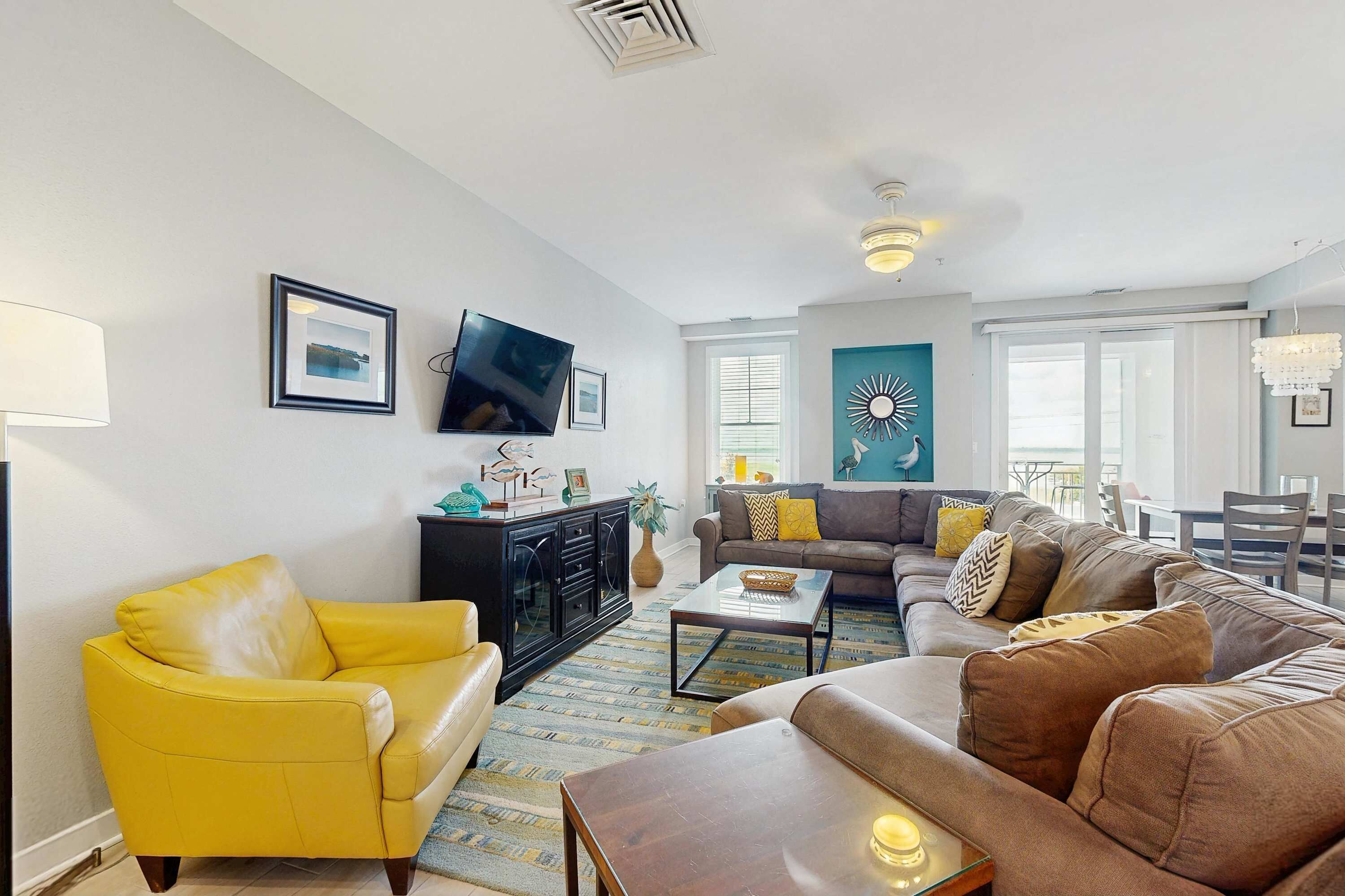A living room with a yellow armchair, a brown sofa, a TV, and a decorative wall piece.