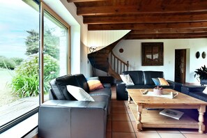 Ein Wohnzimmer mit Holzboden, einer Treppe, einem schwarzen Ledersofa und einem Couchtisch aus Holz.