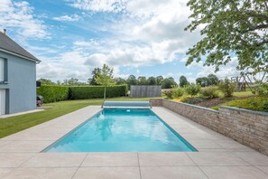 A rectangular swimming pool with a stone border, surrounded by a well-maintained lawn and a hedge. - La Ville Barbier - Belle maison avec piscine (Médréac)