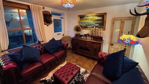 A cozy living room with leather sofas, a patterned rug, a wooden cabinet, and a chandelier. - Cliff View Cottage Holiday Let (Matlock Bath)