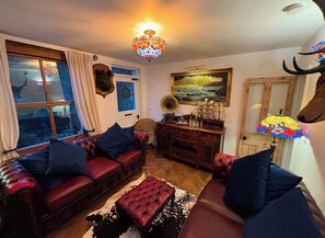 Ein gemütliches Wohnzimmer mit Ledersofas, einem gemusterten Teppich, einer Holzkassette und einer Chandelier.