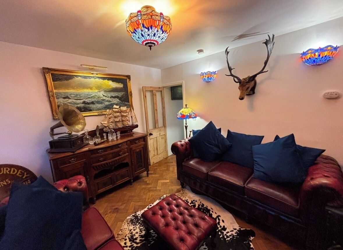A room with a leather sofa, a patterned rug, a wall-mounted deer head, and a painting.