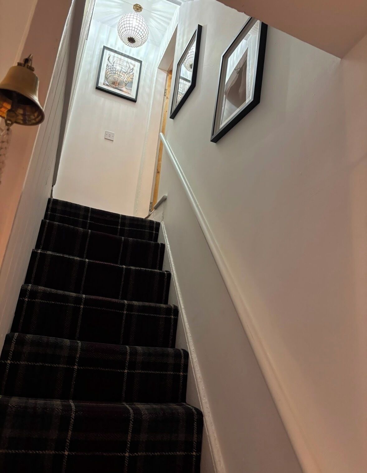 A staircase with a black and white checkered carpet, white walls, and framed pictures on the wall.