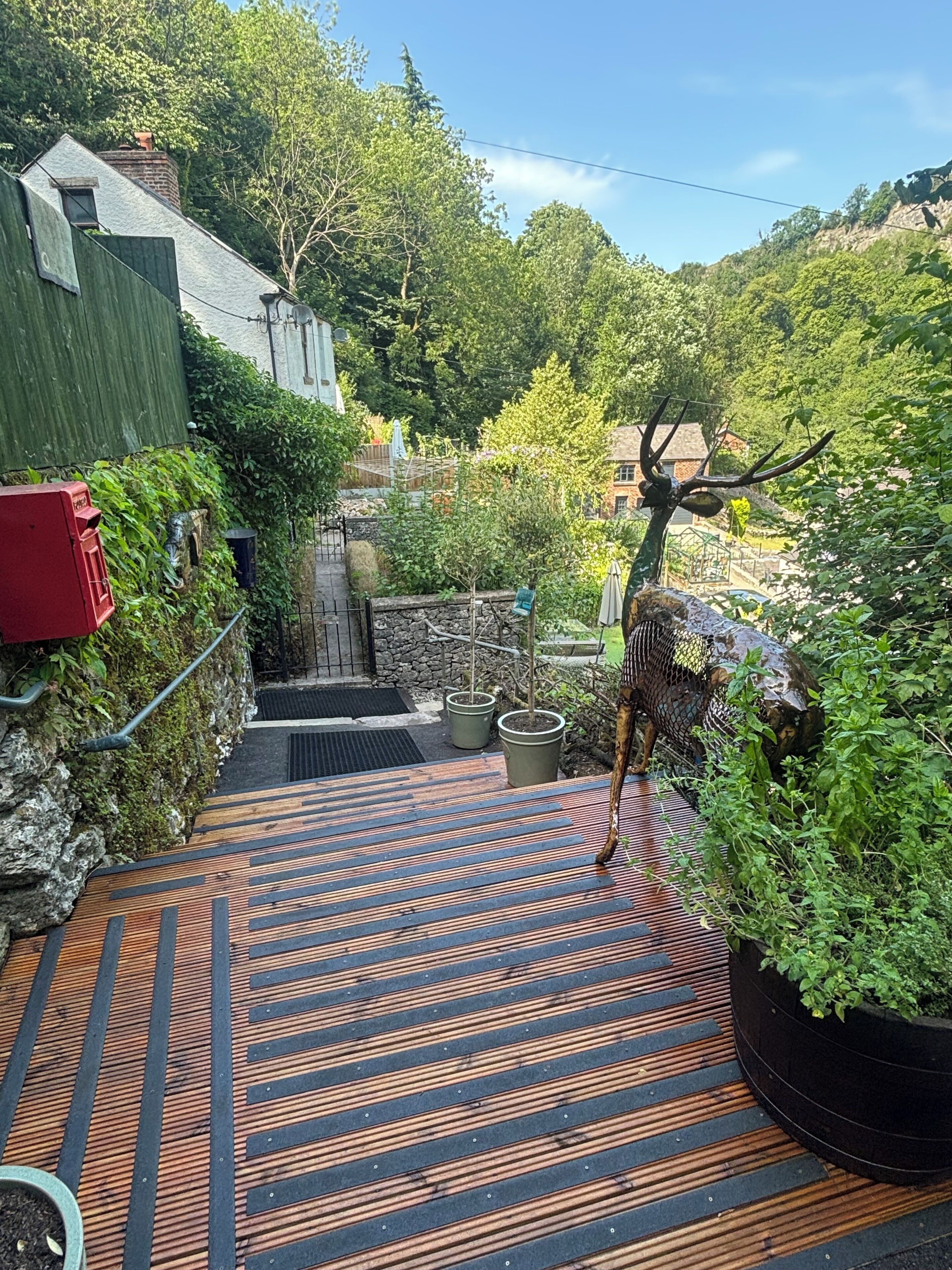 A pathway leading to a house with a green fence, potted plants, and a deer sculpture.