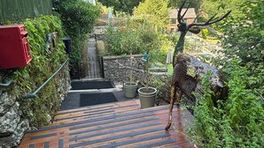 A pathway leading to a house with a green fence, potted plants, and a deer sculpture. - Cliff View Cottage Holiday Let (Matlock Bath)