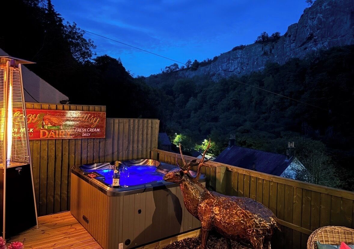 A hot tub on a wooden deck with a deer statue, surrounded by a mountainous landscape.