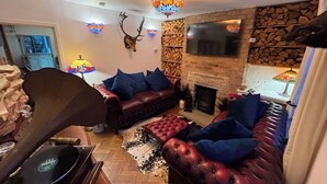 A cozy living room with a fireplace, a leather sofa, and a mounted deer head. - Cliff View Cottage Holiday Let (Matlock Bath)