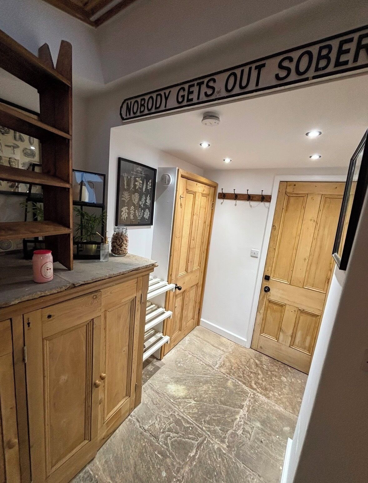 A narrow hallway with wooden doors, a marble floor, and a shelf with various items.
