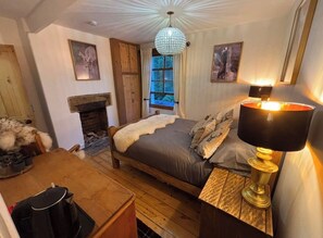 A cozy bedroom with a bed, a fireplace, a dining table, and a chandelier.