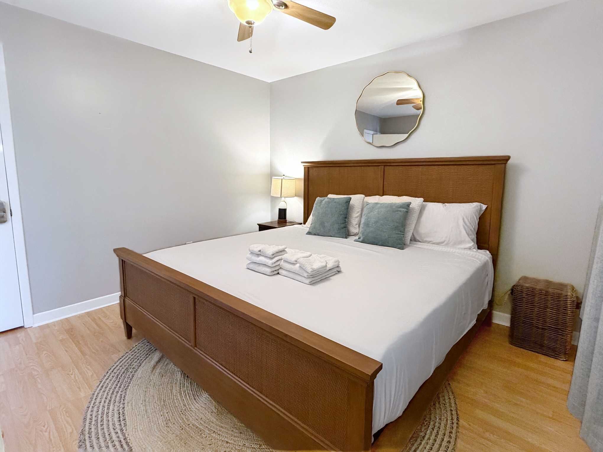 A bedroom with a wooden bed, white bedding, a round mirror, and a nightstand with a lamp.