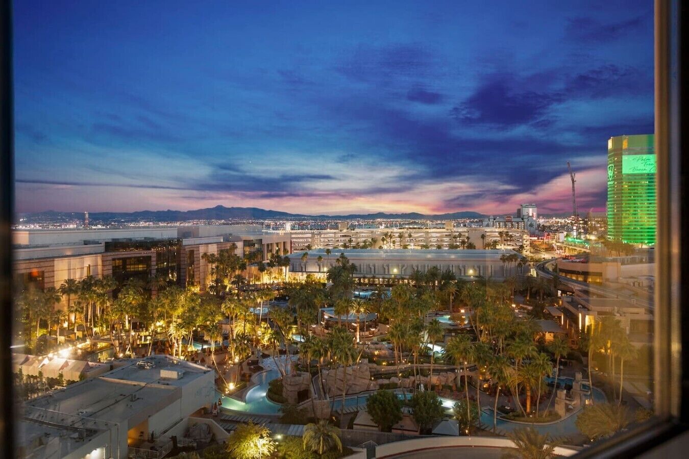 A resort with multiple pools, palm trees, and a cityscape view at dusk.