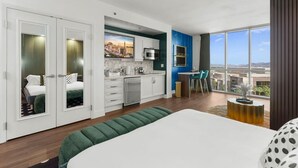 Ein modernes Hotelzimmer mit einem großen Bett, einer Küchenzeile, einem Essbereich mit Stühlen und Blick auf die Stadt.