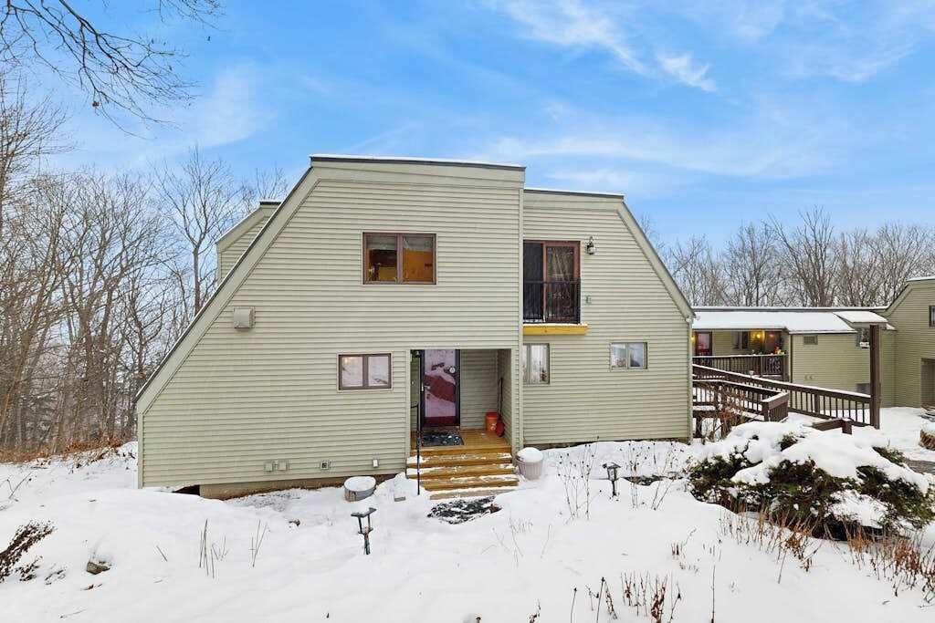 Une maison à deux étages avec un porche à l’avant, un escalier menant à l’entrée et une petite terrasse.