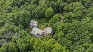 Vista aèria d'una casa aïllada envoltada per un bosc dens, amb una calçada visible i una petita zona de jardí.