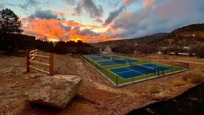 A tennis court with a wooden fence and a large rock in the foreground.