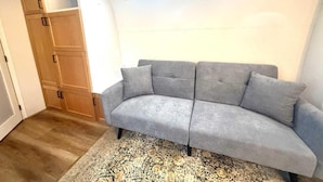 A grey sofa with a patterned rug, wooden wardrobe, and a ceiling light fixture.