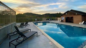 A swimming pool with lounge chairs, a brick building, and a view of hills.