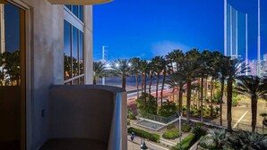 A balcony with a view of palm trees and a cityscape at dusk.