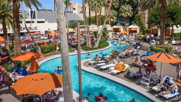 A pool area with lounge chairs, umbrellas, and palm trees.