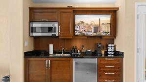 Eine kompakte Küche mit Holzausstattung, einem Edelstahlkühlschrank, einer Mikrowelle, einer Kaffeemaschine und Blick auf die Stadtlandschaft.