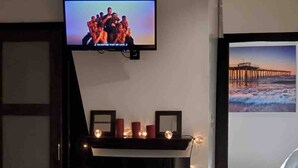 Un televisor montado sobre la chimenea, donde arde fuego, y un cuadro enmarcado en la pared.