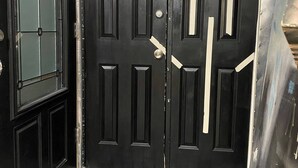 Una puerta negra con cerradura y manija, un panel de vidrio a la izquierda y un piso a cuadros.