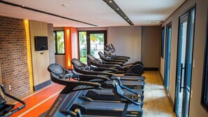 A gym with treadmills aligned along a corridor, a brick wall, and large windows. - Parking Space, View, and Complete Amenities in the City Center | LYVVO (Campinas)
