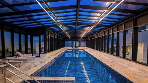 An indoor swimming pool with a glass ceiling, lounge chairs, and a view of the outside. - Parking Space, View, and Complete Amenities in the City Center | LYVVO (Campinas)
